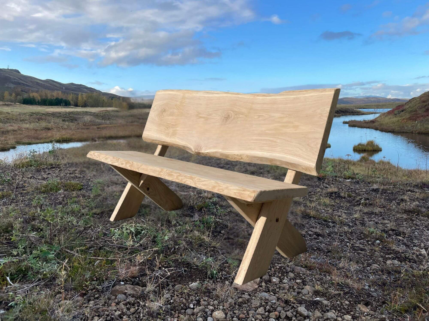 Garðbekkur úr ljósri eik á möl við vatn í íslenskri náttúru – handsmíðaður útibekkur úr harðviði sem þolir íslenskt veður.