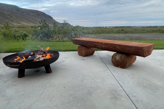 Útihúsgögn Logi bálbekkur úr efnisþykkum viði á steyptum verönd með fjallasýn og eldstæði.